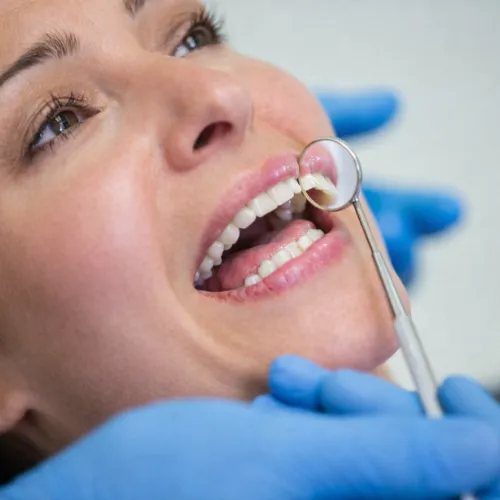 Gloved hands holding dental mirror against woman's teeth.