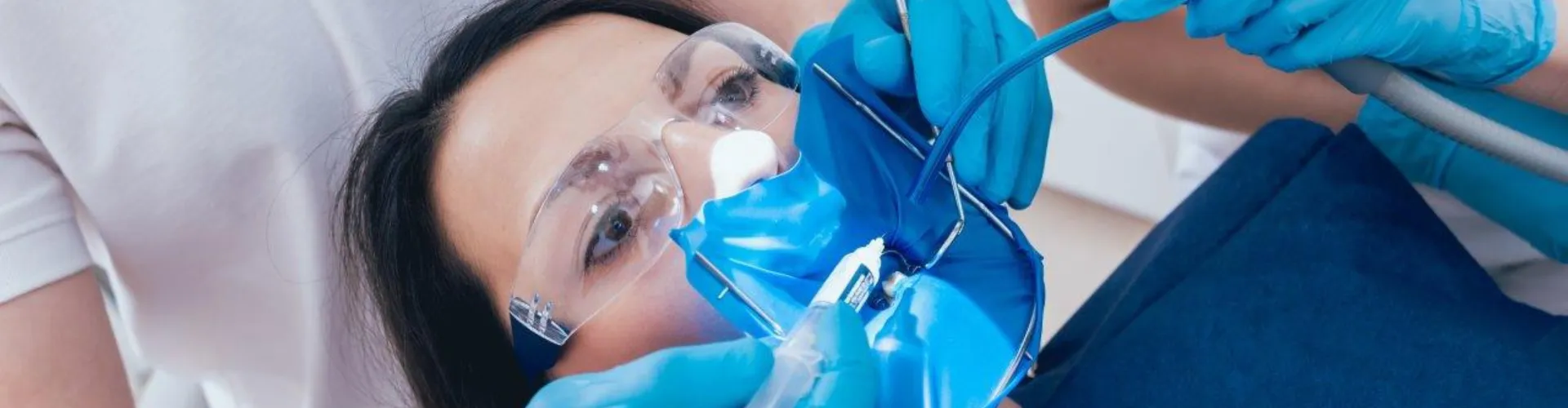 Gloved hands using dental tools in female's mouth.