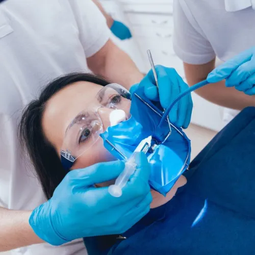 Gloved hands using dental tools in female's mouth.